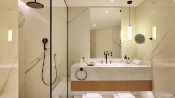 Un baño moderno con ducha envuelta en vidrio, lavamanos de mármol y tocador de madera.