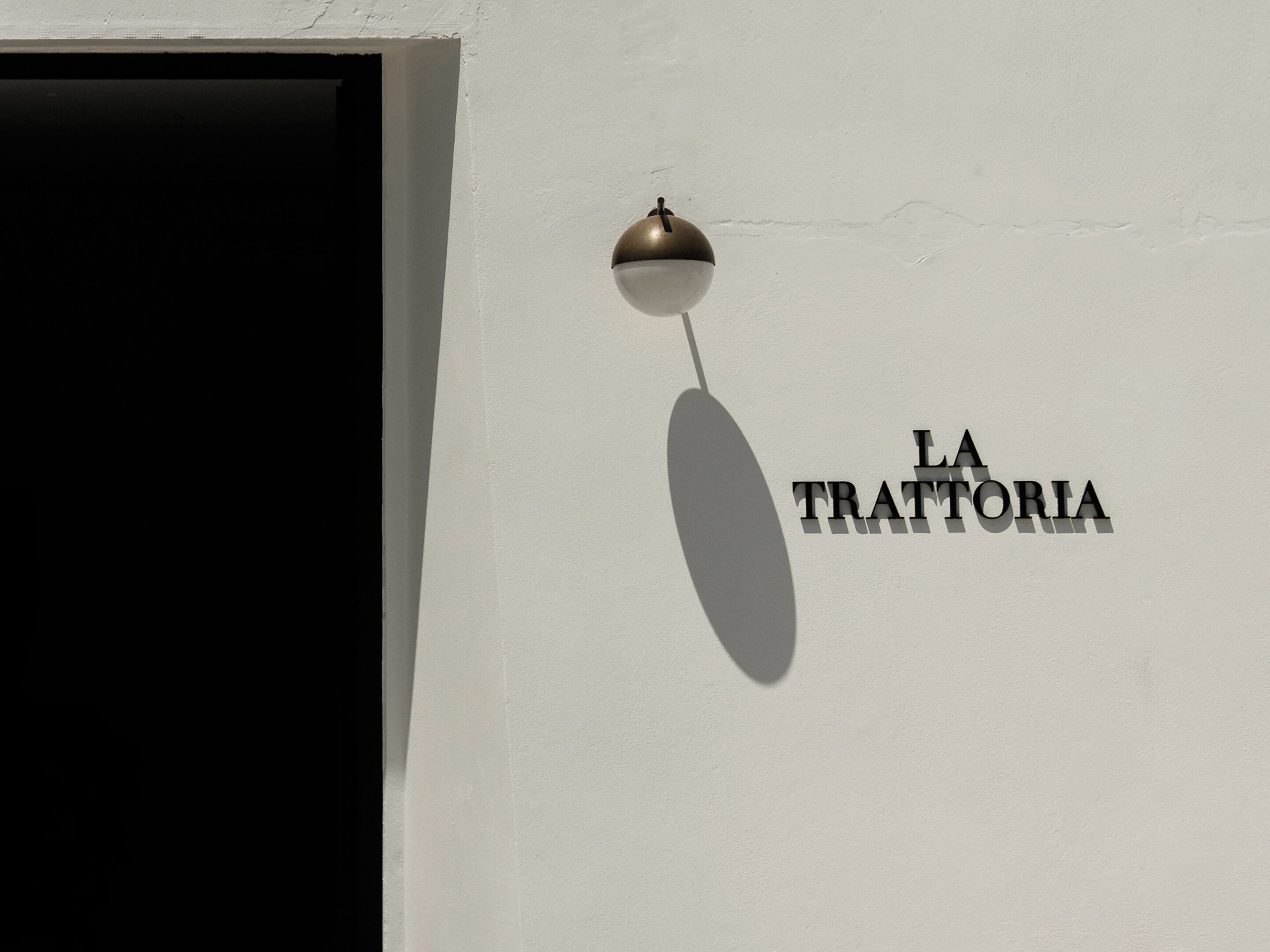 Una pared con el texto 'LA TRATTORIA' y una lámpara colgante.