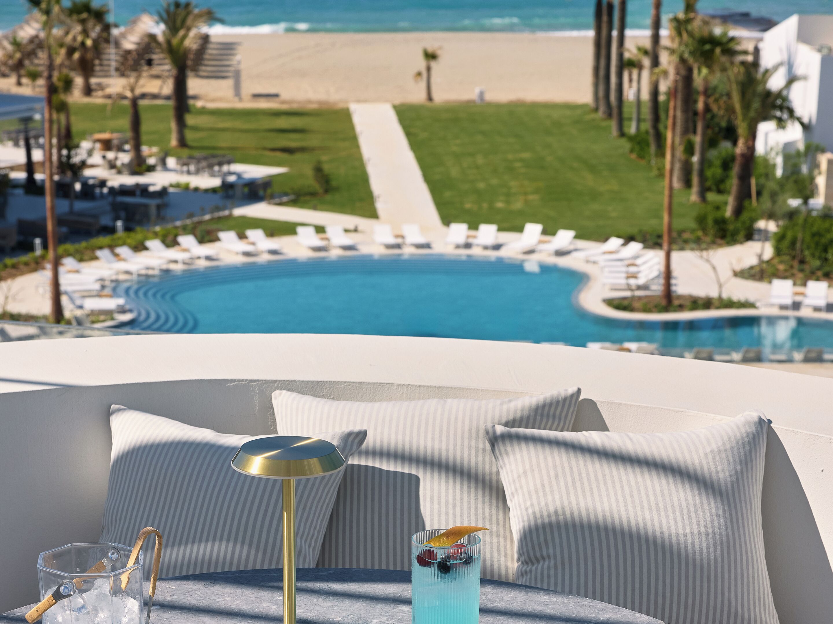 Une vue sur la piscine, avec des chaises longues, la piscine elle-même et une plage en arrière-plan.
