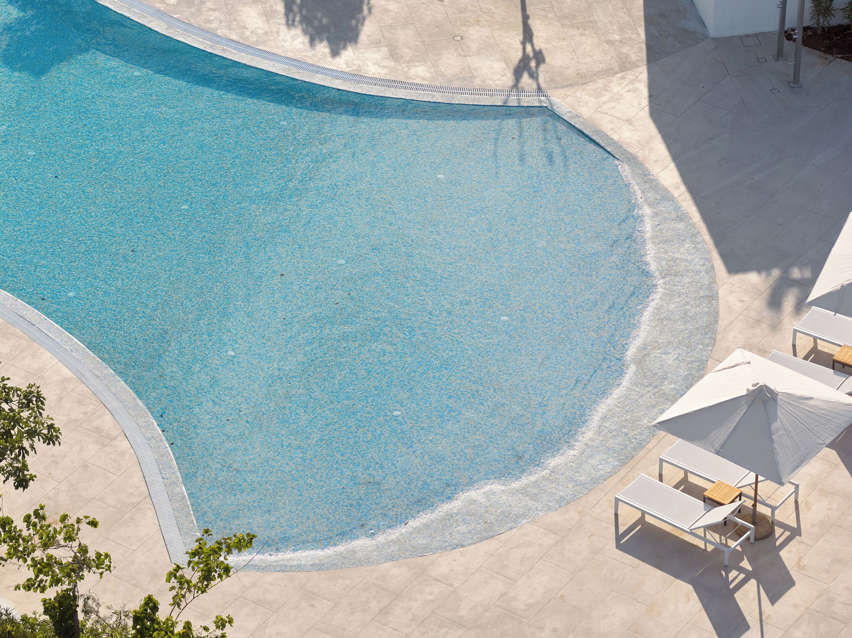 A swimming pool with a curved edge, surrounded by a tiled deck and outdoor seating.
