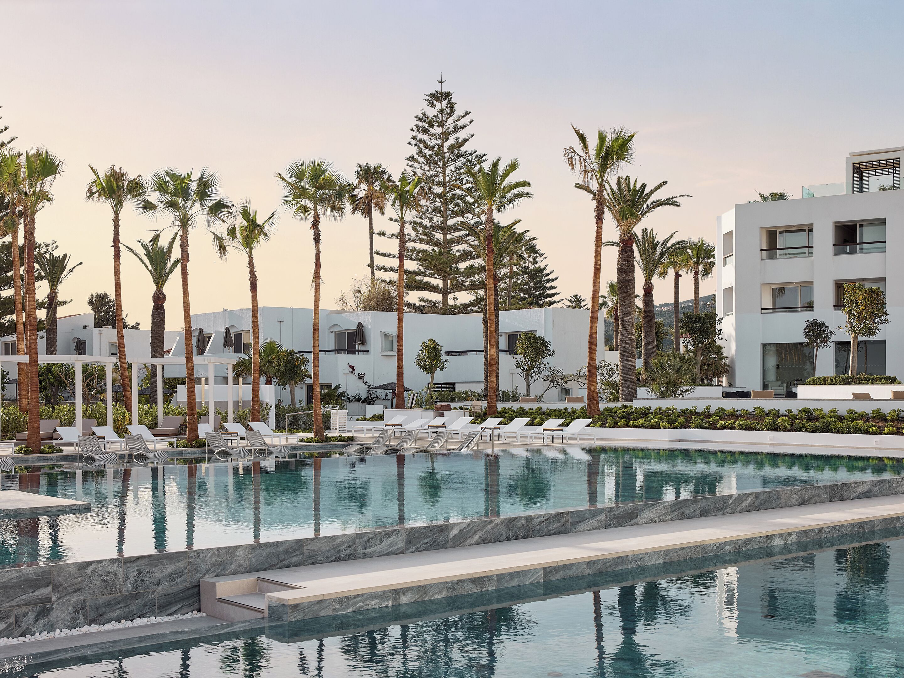 A pool area with lounge chairs, palm trees, and modern buildings.