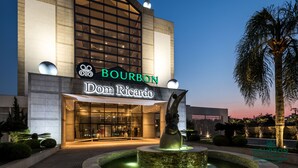 Un bâtiment moderne doté d’une grande façade en verre, d’une enseigne bien visible indiquant « Bourbon Dom Ricardo », et d’une fontaine centrale.