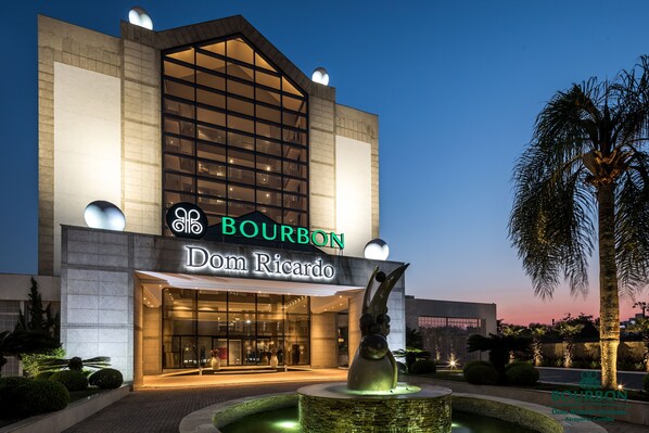 Un bâtiment moderne doté d’une grande façade en verre, d’une enseigne bien visible indiquant « Bourbon Dom Ricardo », et d’une fontaine centrale.