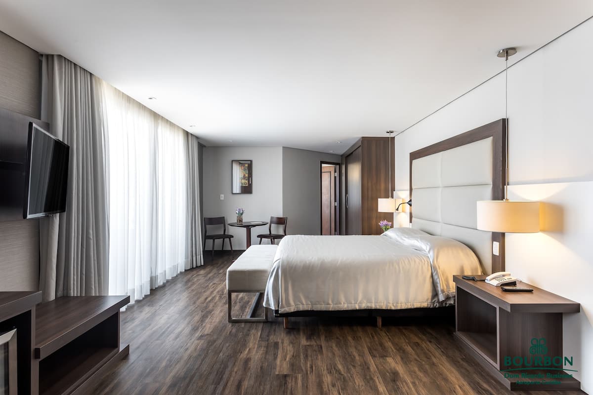 Une chambre d’hôtel comprenant un lit, une table de chevet, une lampe, une télévision et un bureau avec des chaises.
