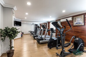 Une salle de sport équipée de tapis de course, de vélos elliptiques et d’un vélo d’appartement. On y trouve une plante en pot et un téléviseur fixé au mur.
