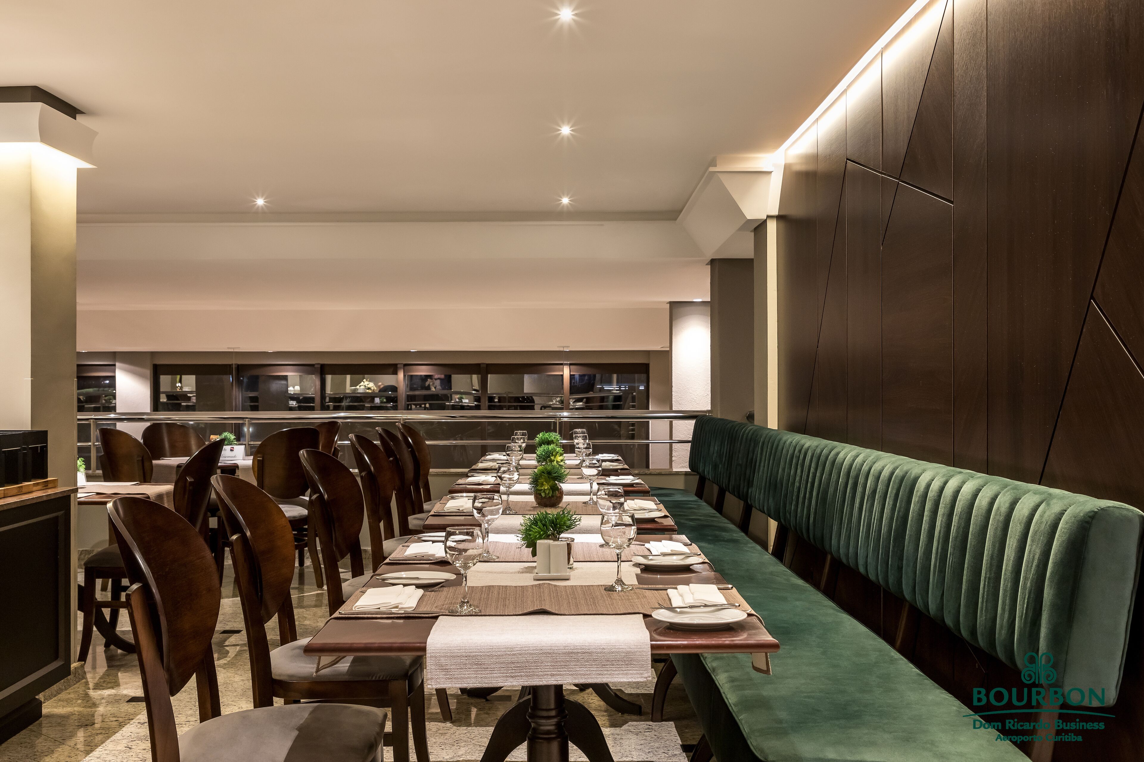 A modern dining area with a long table, chairs, and a green upholstered bench.