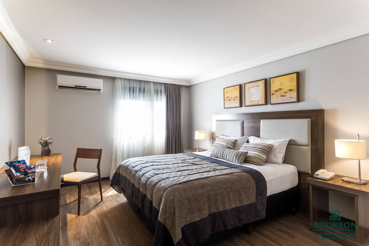 Een moderne hotelkamer met een groot bed, nachtkastjes, een bureau met een laptop en een stoel.