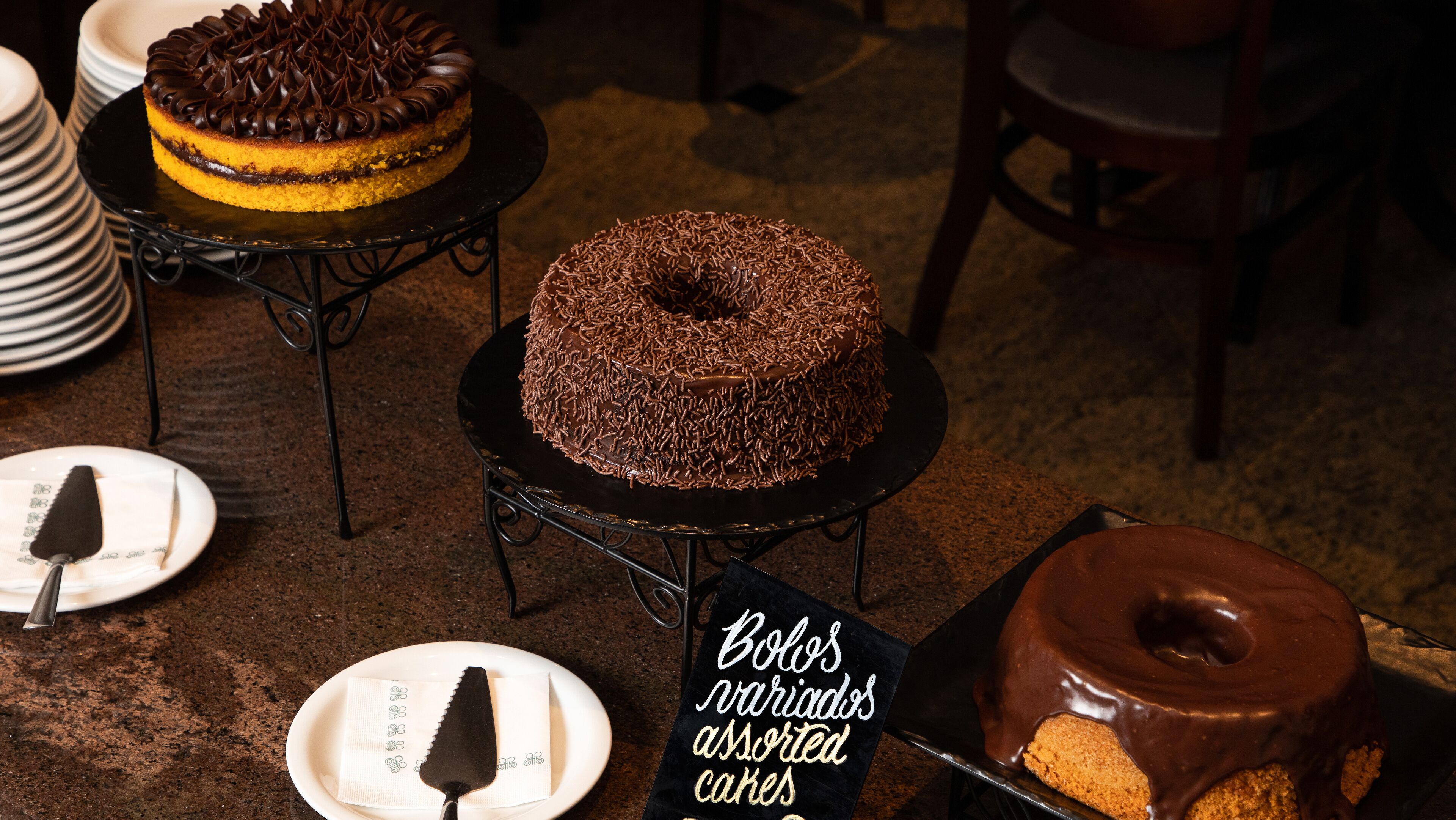 A selection of cakes on display, including a chocolate cake with sprinkles and a yellow cake with chocolate frosting.