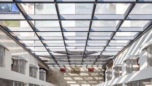 Un intérieur d’hôtel moderne avec un plafond en verre, des rampes en métal et un couloir central.