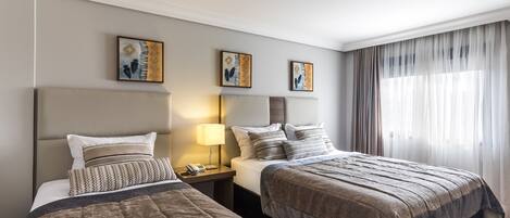 Habitación de hotel con dos camas, una mesita de noche, una lámpara y obras de arte en la pared.
