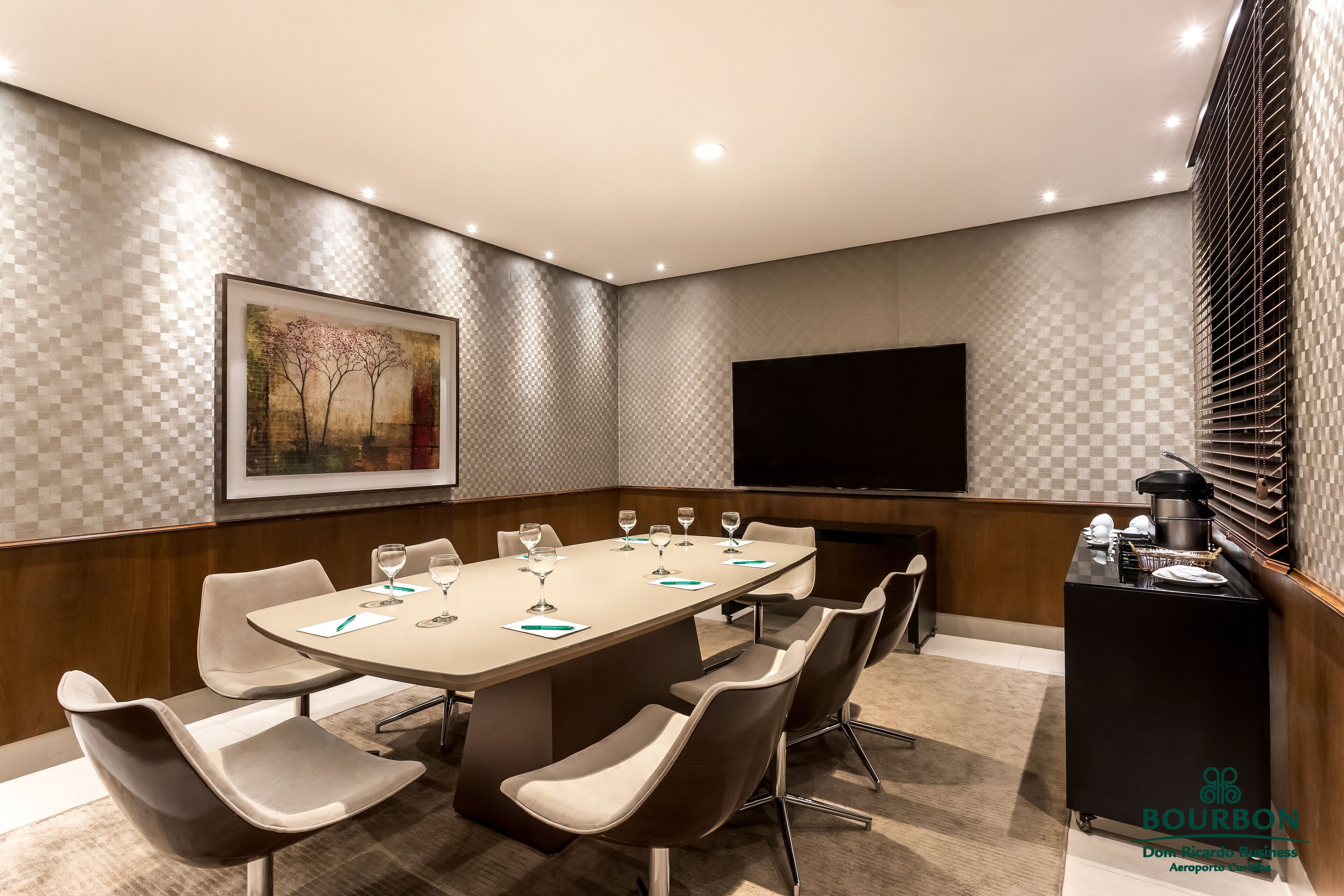 Een vergaderzaal met een grote tafel, stoelen, een flatscreen-tv en een minibarsce.