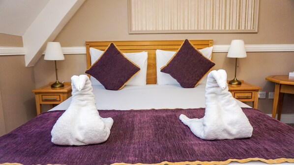 A hotel room with a bed, two nightstands, a lamp, and a window with blinds. - Ashbourne Court Hotel (Ashbourne)
