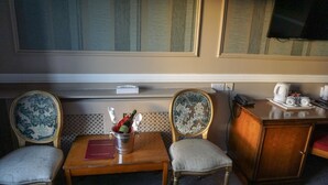 Et hotelværelse med et træbord, to polstrede stole, et lille skab og et fjernsyn ophængt på væggen.