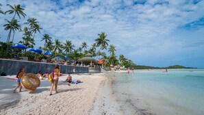 A beach with palm trees, umbrellas, and people relaxing.