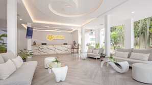 A modern hotel lobby with a marble reception desk, plush seating, and a large window overlooking greenery.