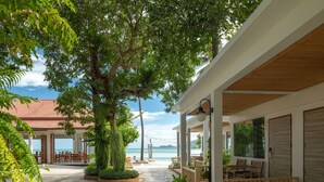 A covered outdoor area with a dining setup, a large tree, and a view of the sea.