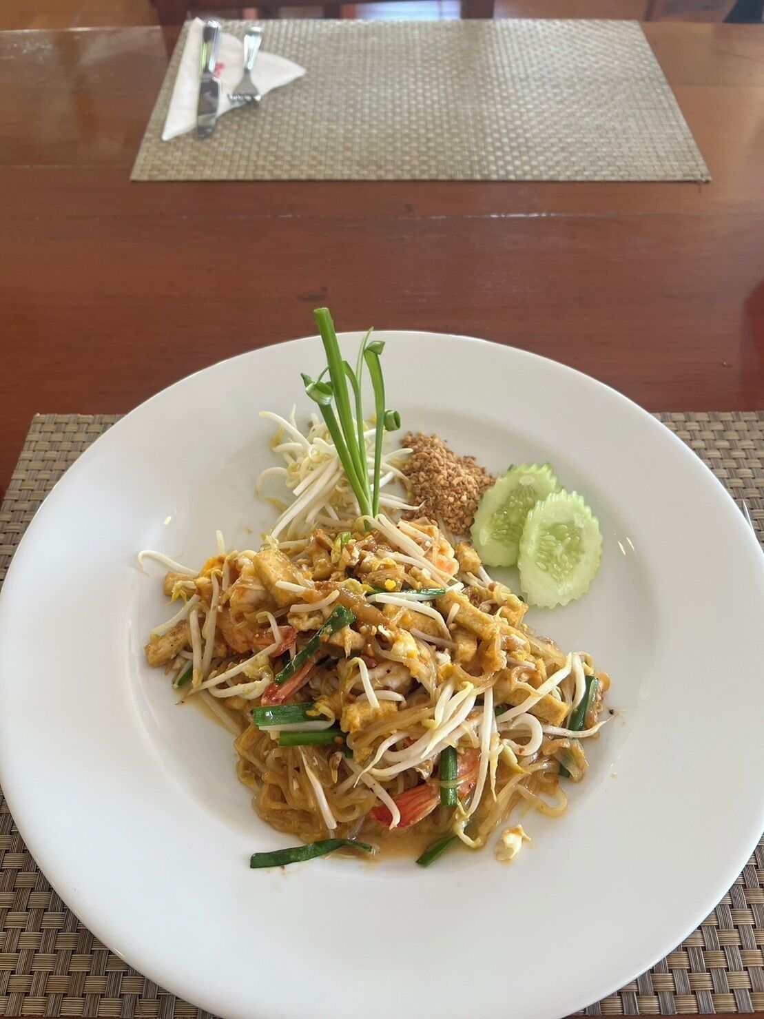 A plate of Pad Thai with bean sprouts, green onions, and cucumber slices on a white plate.