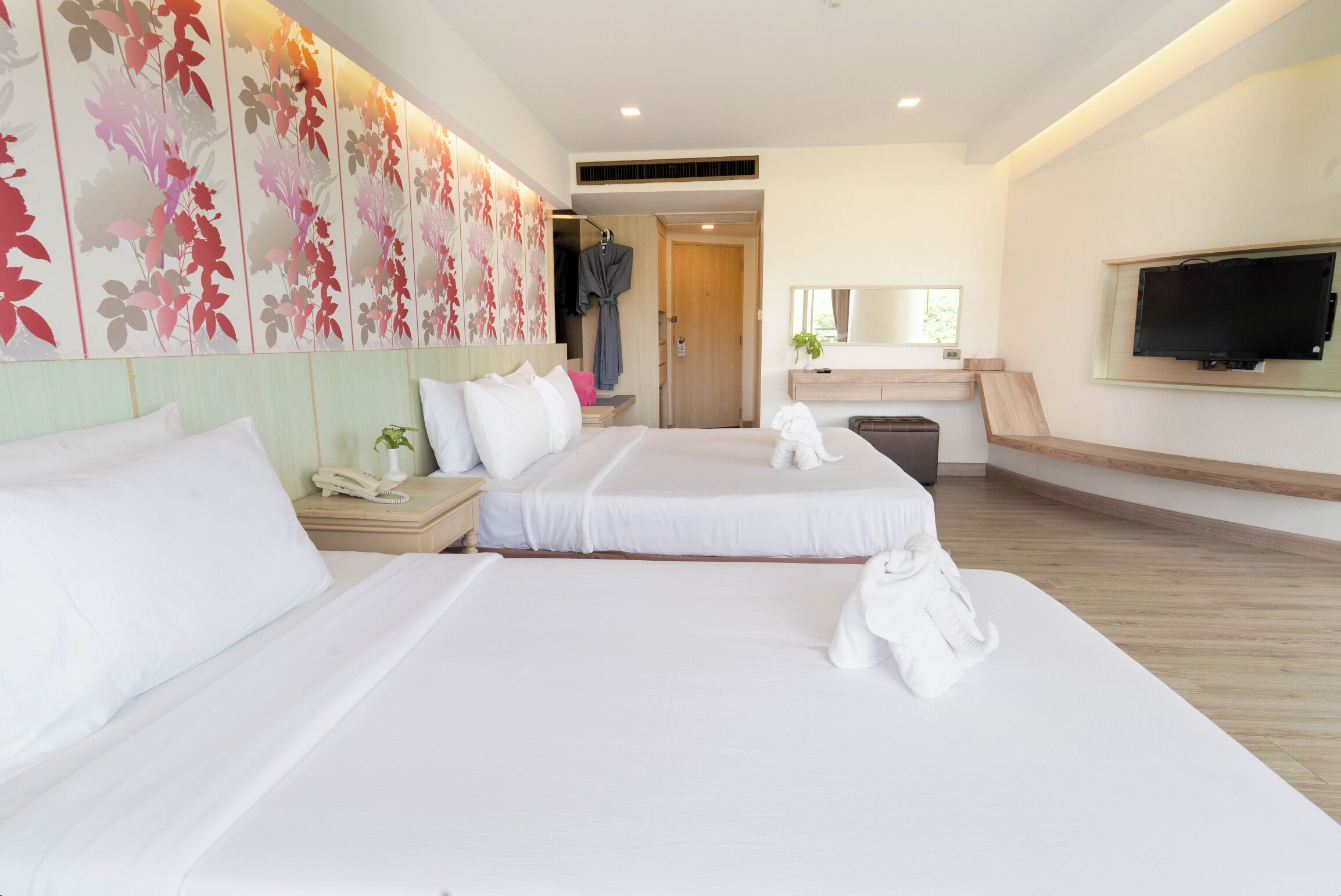 A hotel room with two beds, a TV, a mirror, and a floral wall.