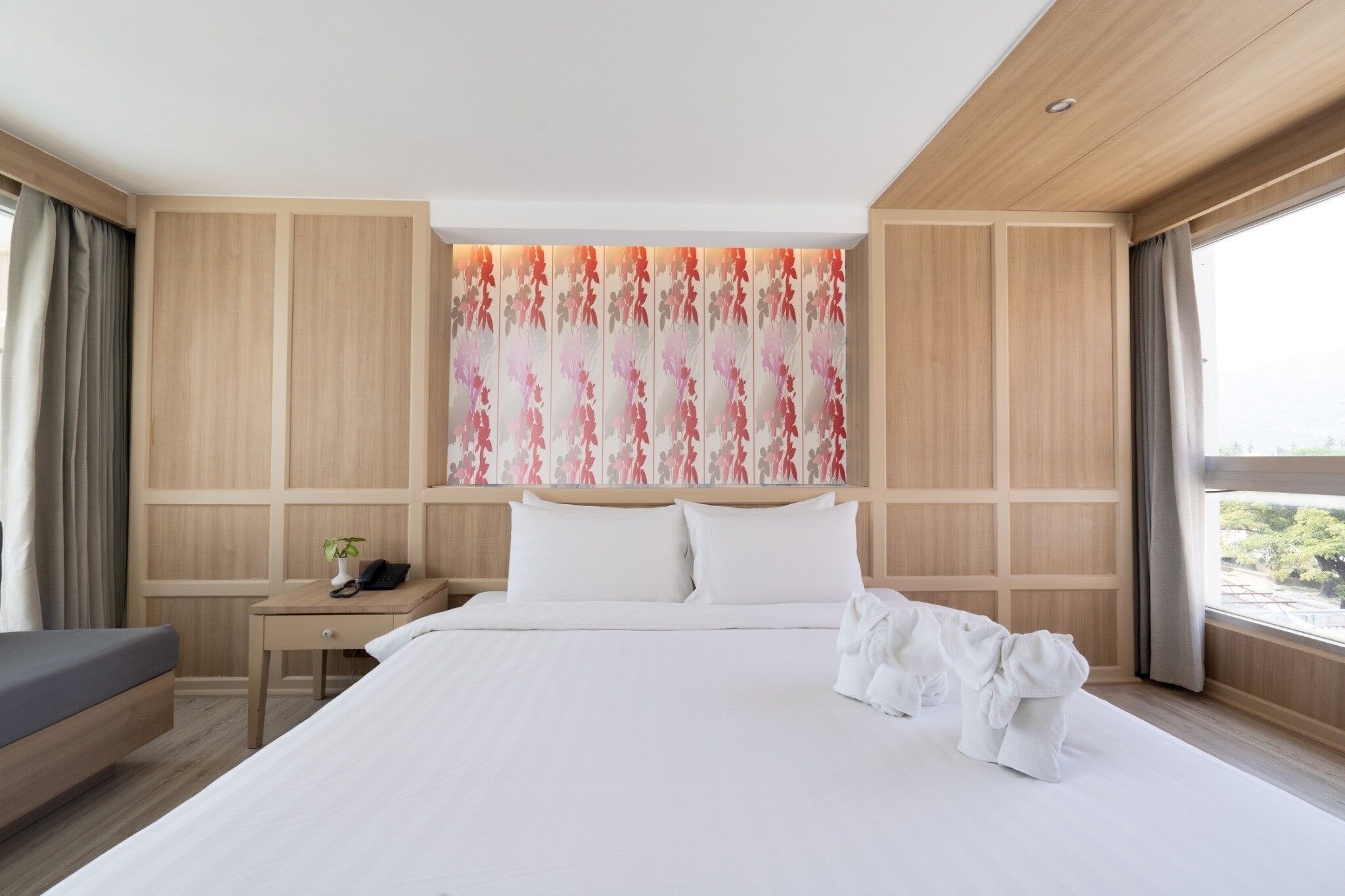 Ein modernes Hotelzimmer mit einem großen Bett, Nachttischen, einem kleinen Schreibtisch und einem Fenster mit Vorhängen.