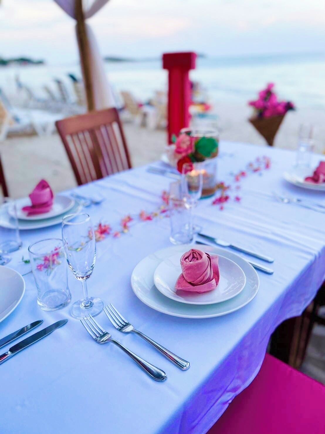 Een eettafel aan het strand, gedekt met borden, glazen en bestek, met uitzicht op zee.