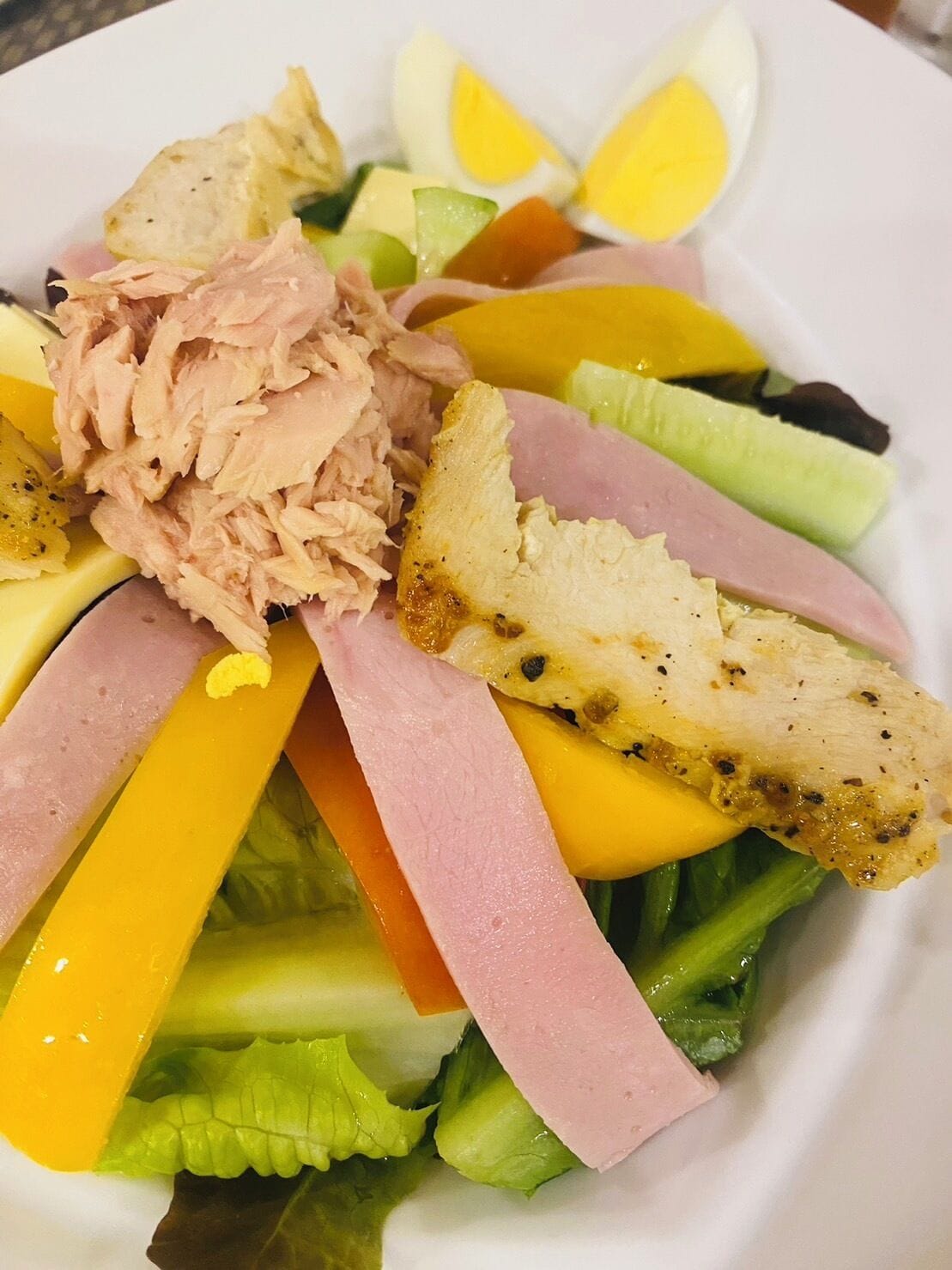 Ensalada con varios ingredientes, incluyendo lechuga, jamón en rodajas, atún y huevos duros.