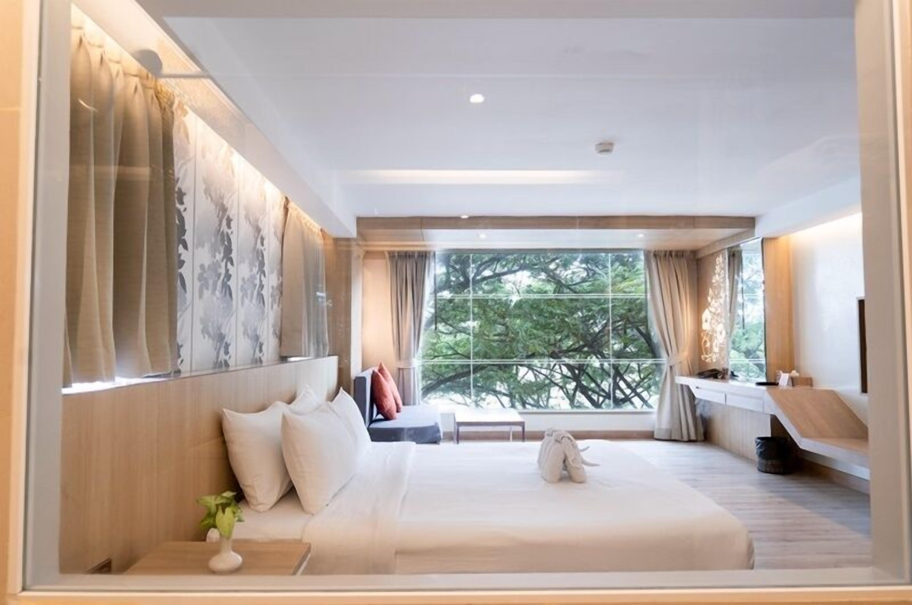 Une chambre d’hôtel moderne dotée d’un grand lit, d’une table de chevet, d’une fenêtre donnant sur les arbres et d’un bureau intégré avec une chaise.