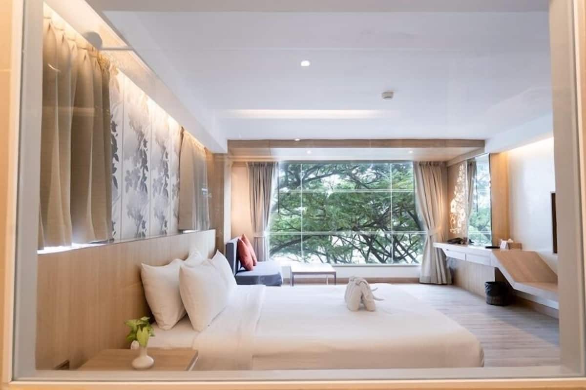Une chambre d’hôtel moderne dotée d’un grand lit, d’une table de chevet, d’une fenêtre donnant sur les arbres et d’un bureau intégré avec une chaise.