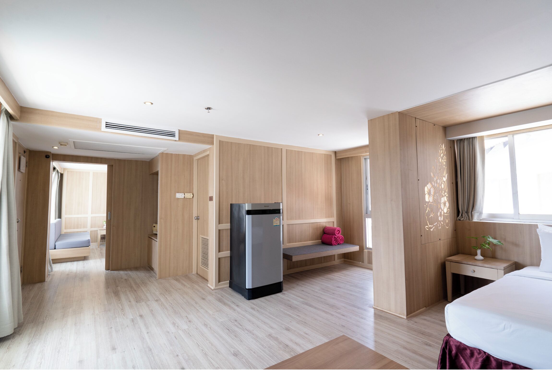 A modern hotel room with a bed, a small desk, a seating area, and a built-in refrigerator.
