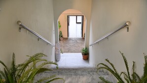 A staircase with metal handrails, a potted plant at the bottom, and a doorway leading to an open space. - Avra (Agios Vasileios)