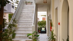 A corridor with a marble staircase, potted plants, and a hanging light fixture. - Avra (Agios Vasileios)