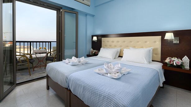 A hotel room with a bed, a nightstand, a lamp, a chair, and a balcony with a table and chairs. - Avra (Agios Vasileios)