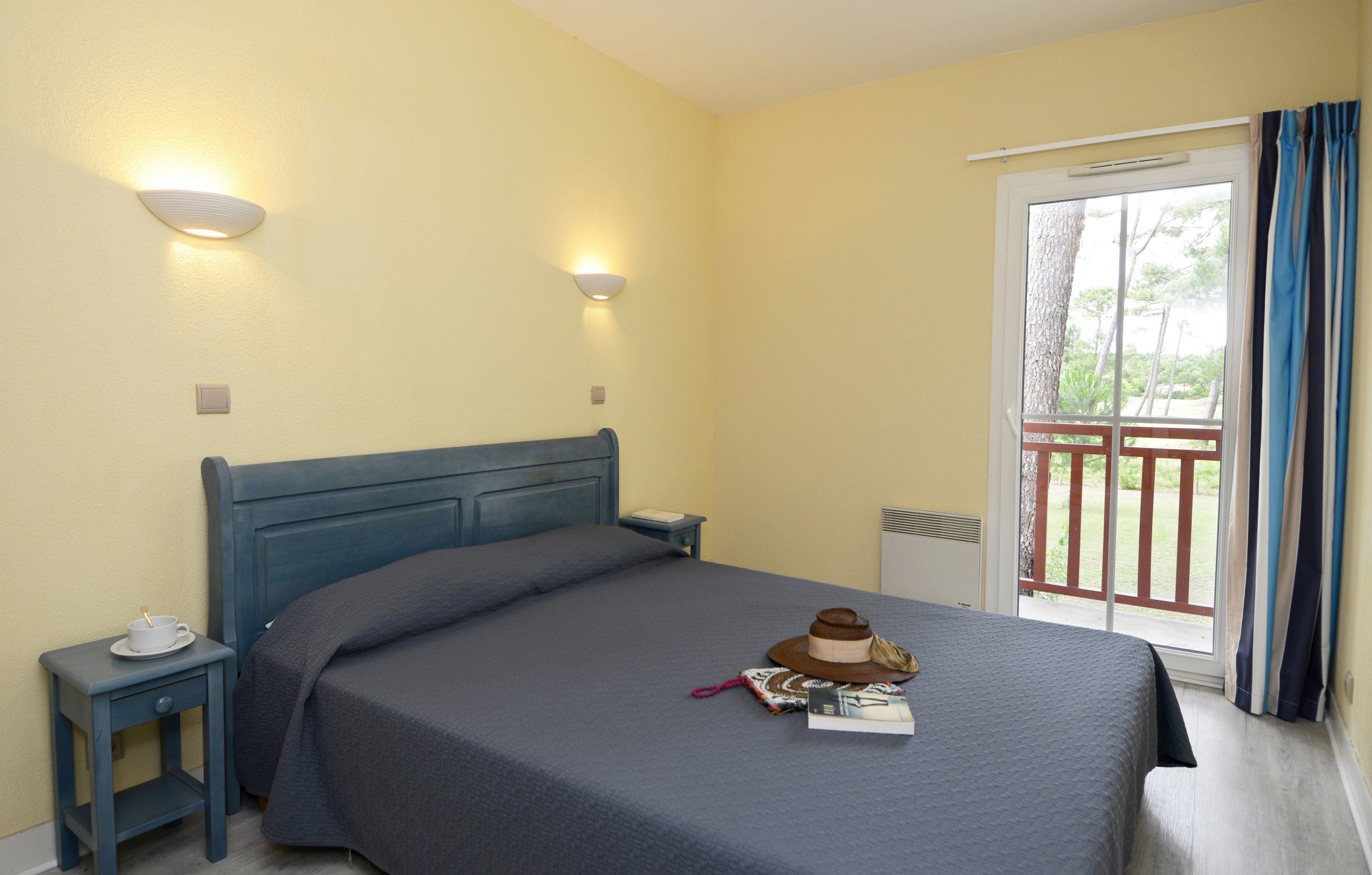 A bedroom with a bed, bedside tables, a nightstand, a hat, a book, and a window with curtains.