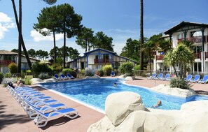 A swimming pool with lounge chairs, a building with a blue and white facade, and surrounding trees.