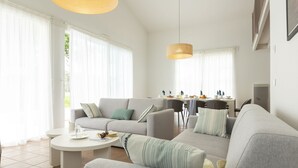 Un salon spacieux avec un canapé gris, une table basse ronde et, au fond, un coin repas.