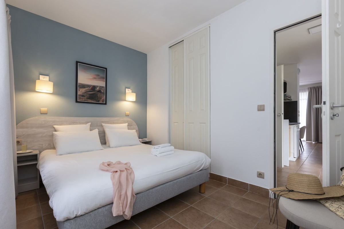 Un lit bien fait, avec du linge de lit blanc, une tête de lit et deux lampes fixées au mur.