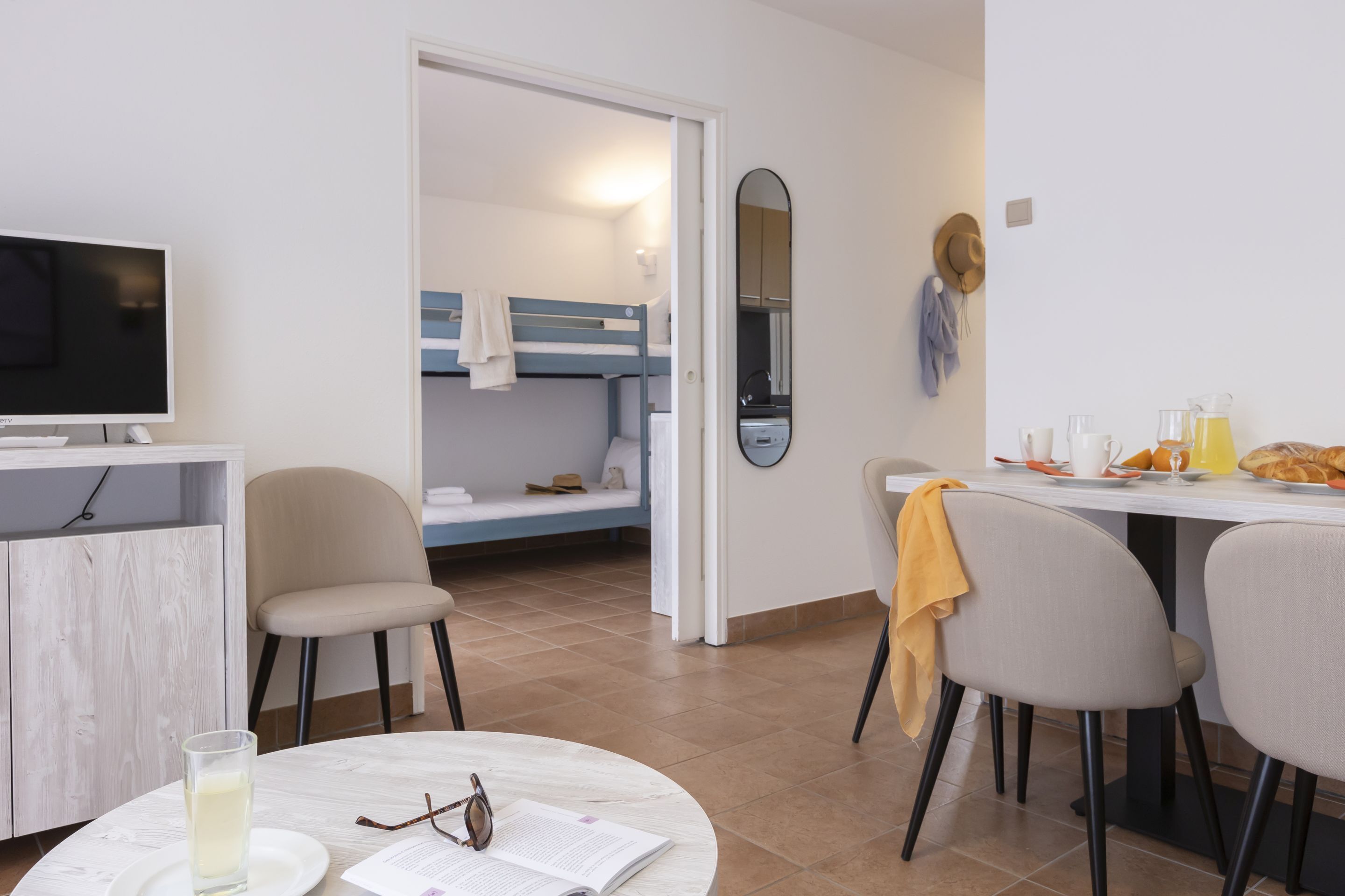 A modern room with a bunk bed, a dining table with chairs, a TV, and a small kitchen area.