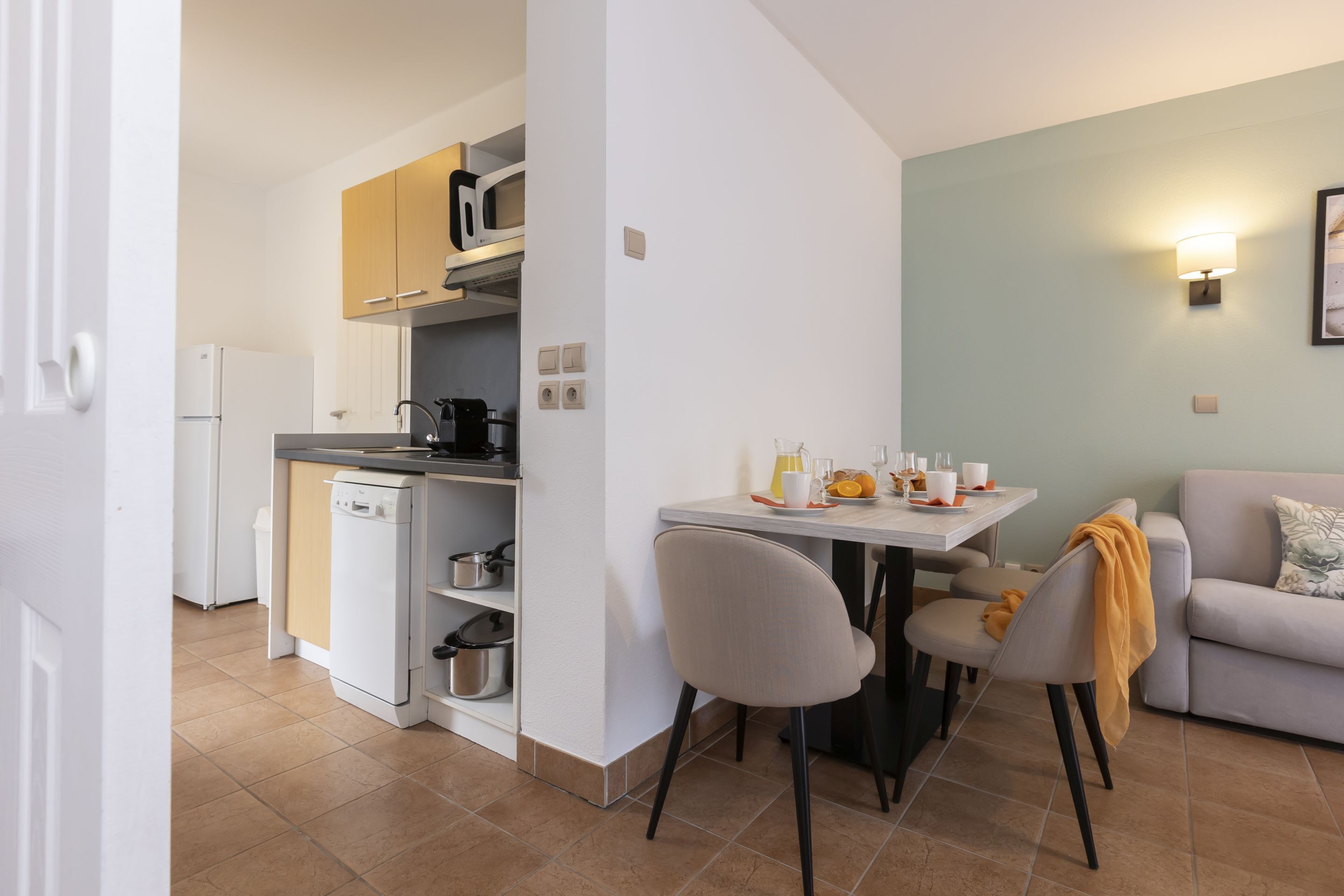 Una cocina funcional con lavavajillas, microondas y cafetera. Hay una mesa de comedor con sillas y un sofá en la zona de estar.