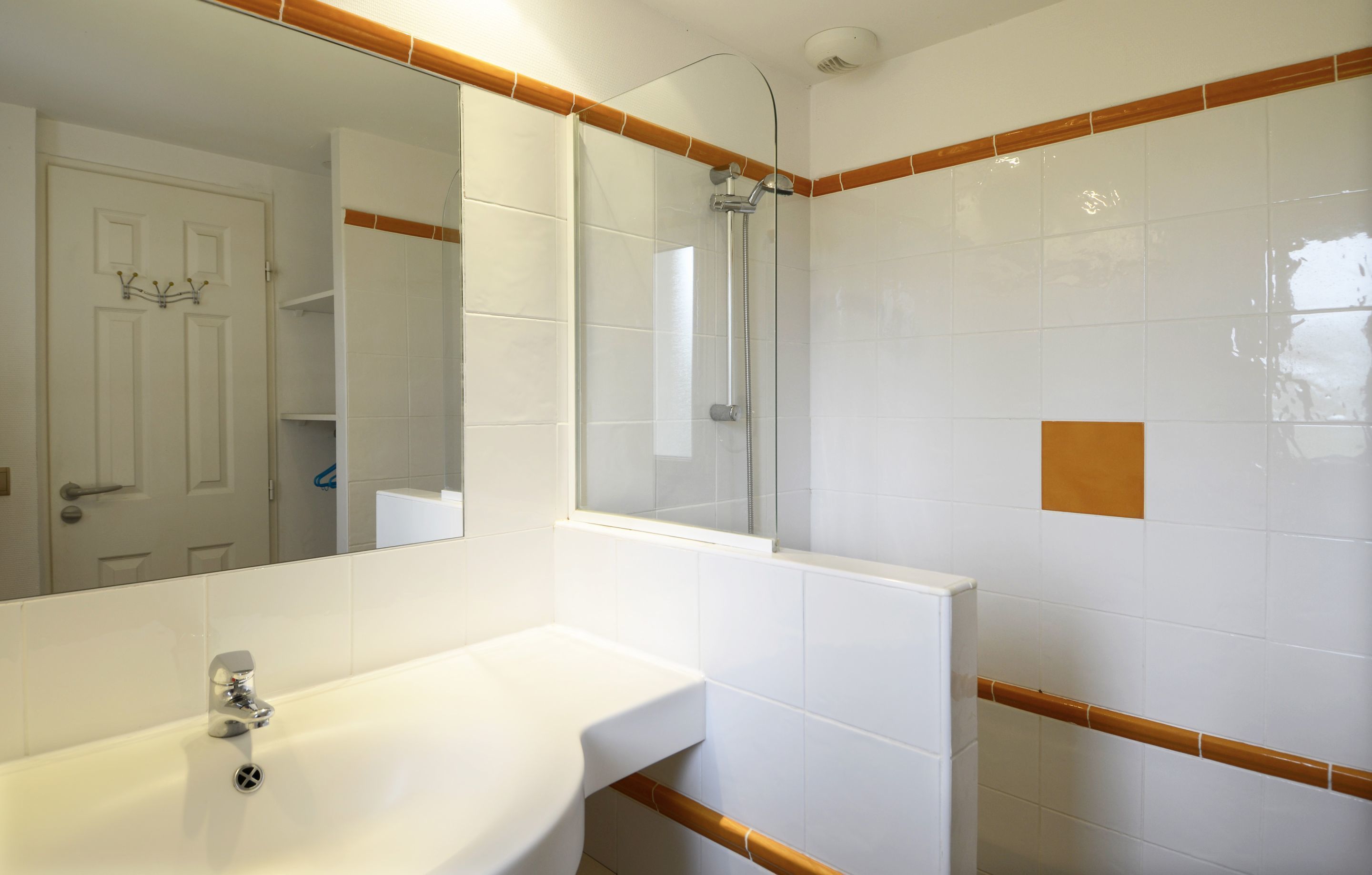 Une salle de bain avec un lavabo blanc, une cabine de douche en verre et un miroir.