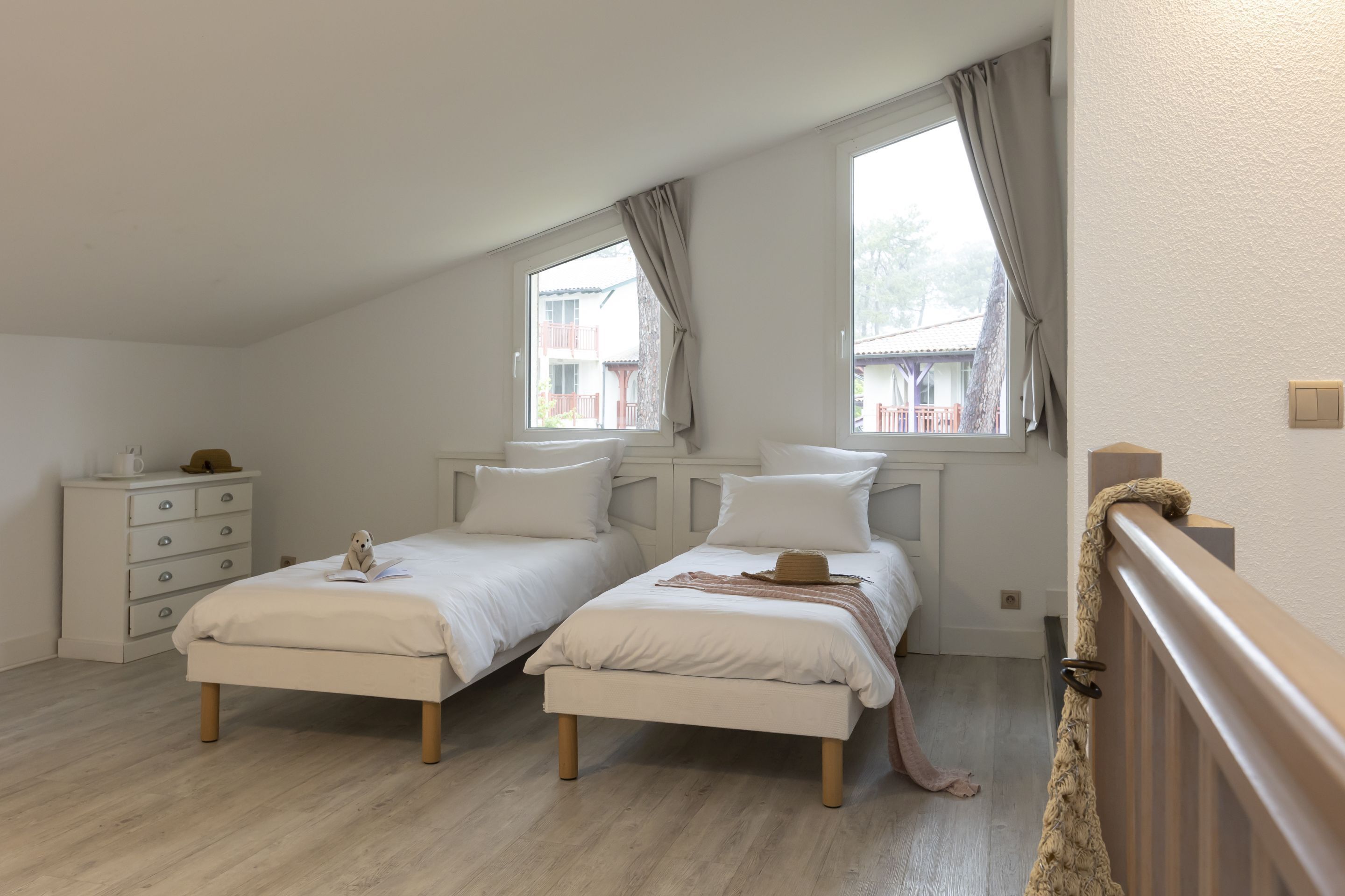 A bedroom with two beds, a dresser, and a window with curtains.