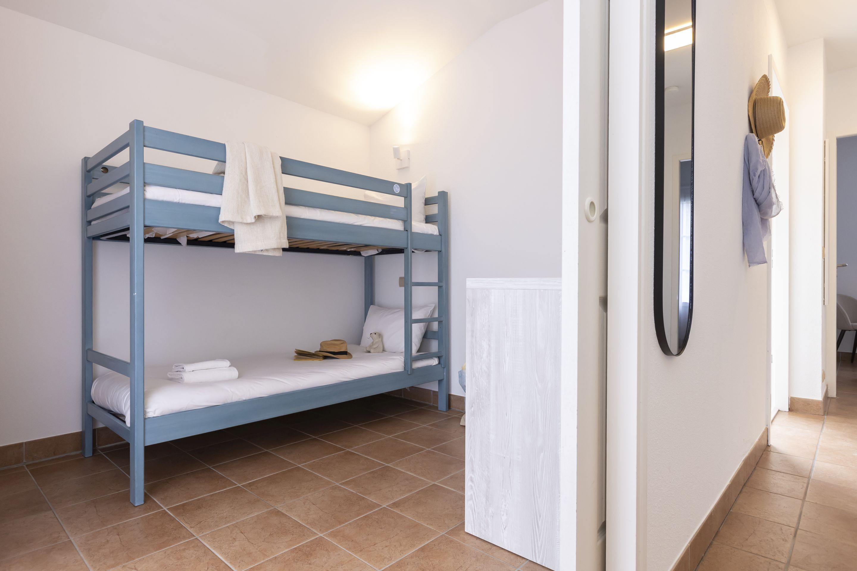 A bunk bed with a white mattress, a towel, and a hat hanging on the wall.
