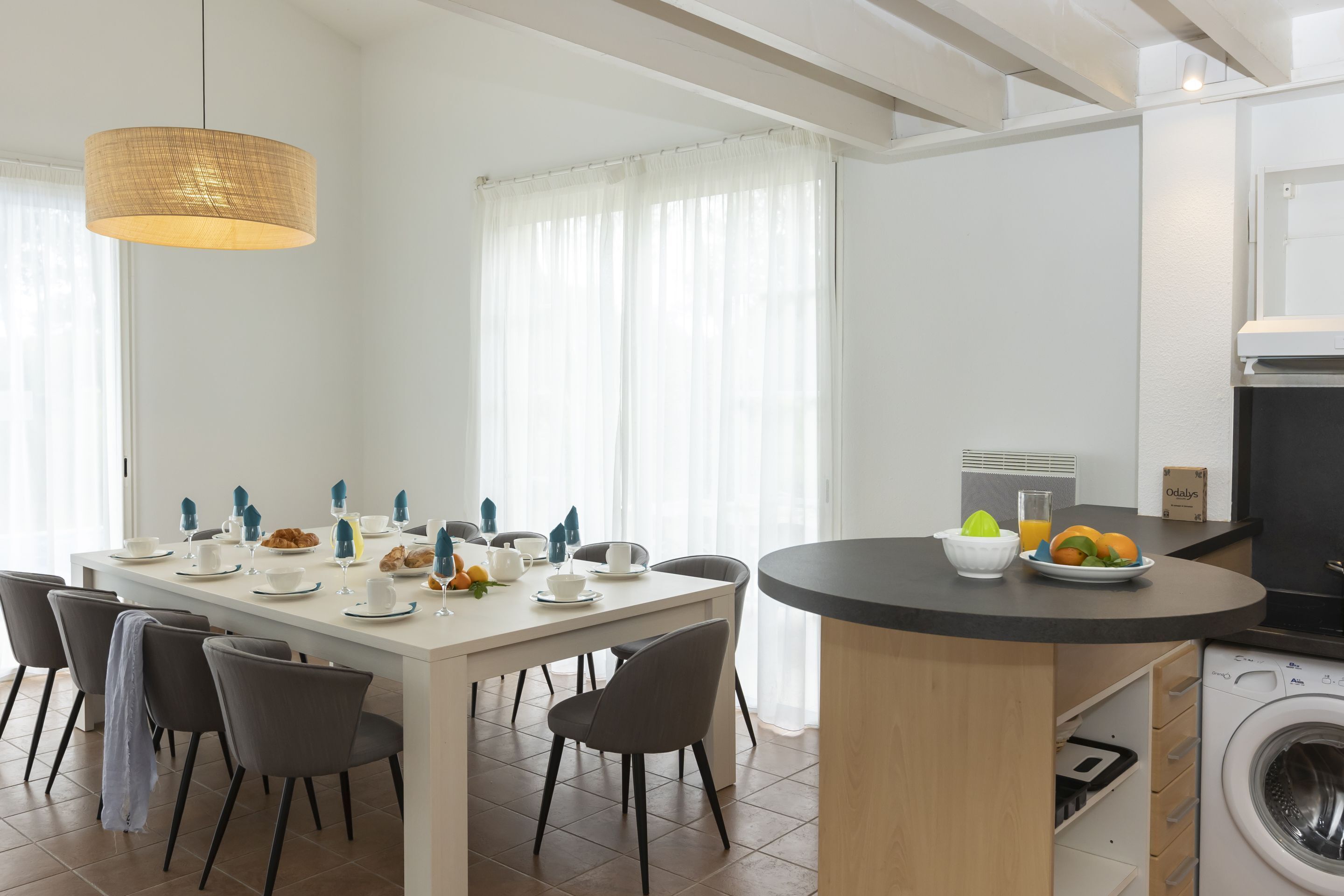 A modern kitchen with a built-in washing machine, a dining area with a white table and chairs, and a hanging light fixture.