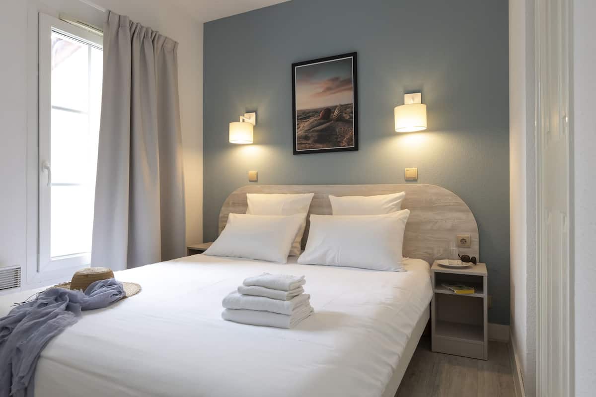 A neatly made bed with white linens, a headboard, two bedside lamps, a nightstand with a glass of water, and a framed picture on the wall.