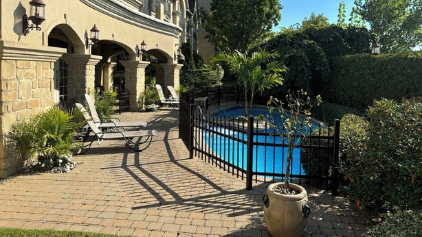 Un área de piscina con una piscina azul, rodeada por un sendero de ladrillos y una gran jardinera de piedra.