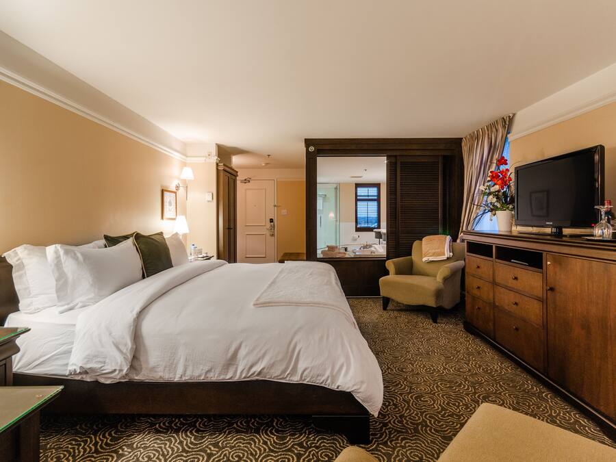 A hotel room with a large bed, a television, a desk, and a dresser.