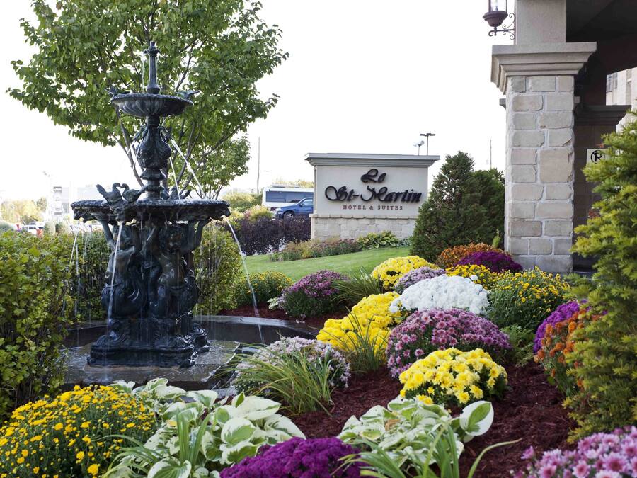 A fountain surrounded by colorful flower beds and a sign for 'The Martin Hotel & Suites'.