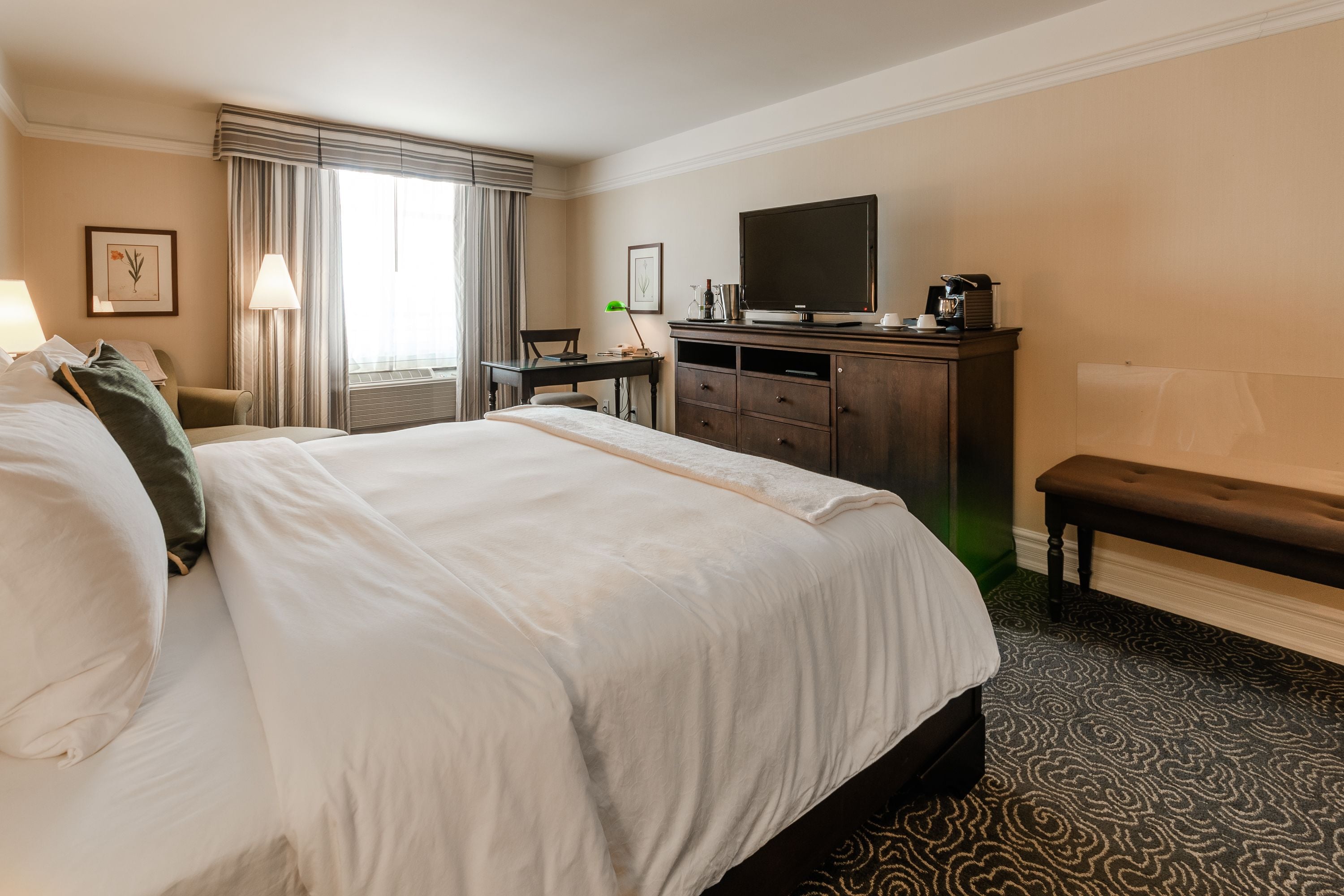 Una habitación de hotel con una cama grande, un escritorio con computadora, un televisor y una banca.
