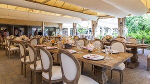 Un área de comedor al aire libre con mesas y sillas de madera, cubierta por un toldo.