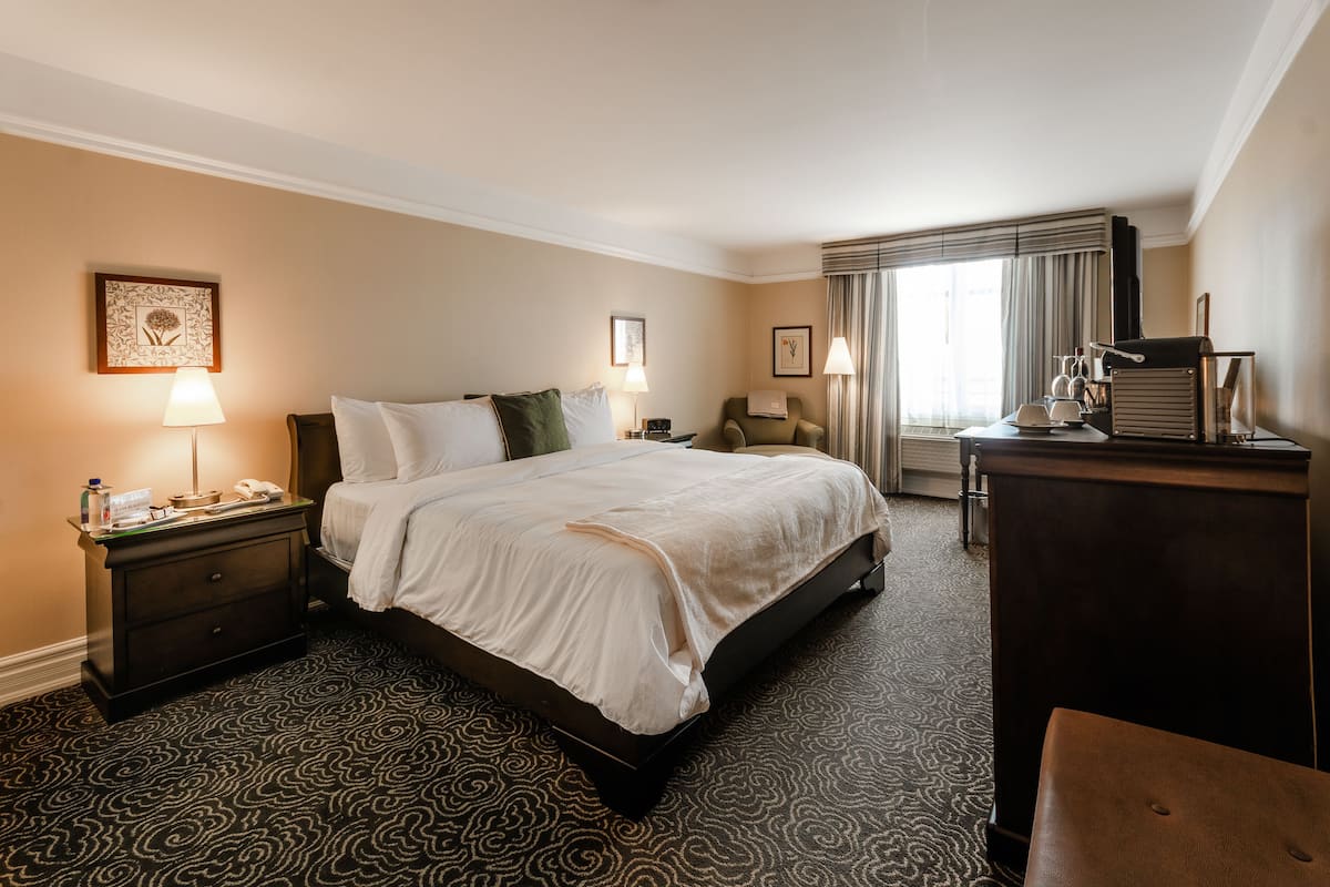 Una habitación de hotel con una cama grande, un escritorio, una silla y un aparador.