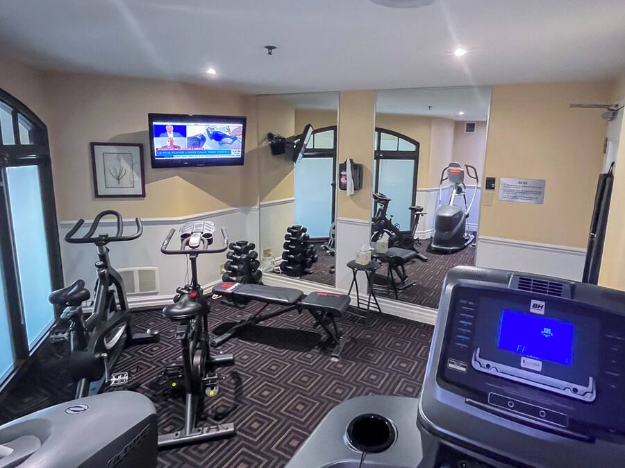 Ett gym med träningsutrustning, en tv och en vägg med speglar.