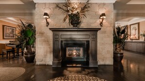 Una chimenea con repisa de piedra, flanqueada por dos apliques de pared, en una habitación con un piano y plantas en macetas.